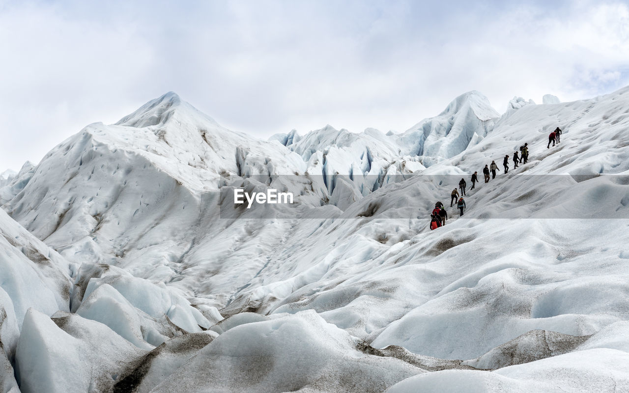 Low angle view of people climbing on glacier against sky