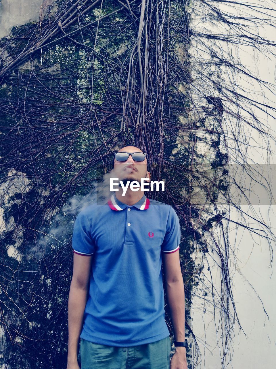 Man exhaling smoke while standing against creeper plants