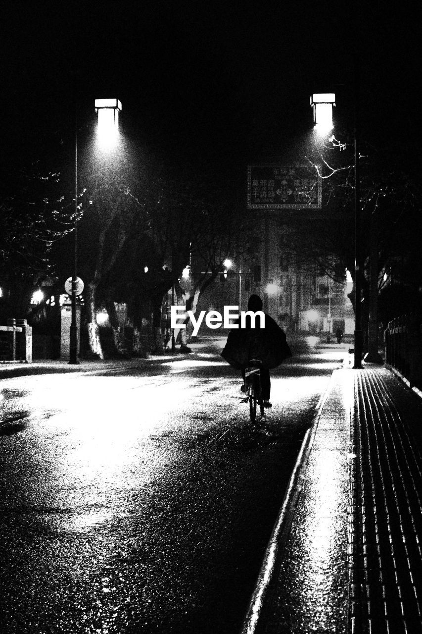 SILHOUETTE OF MAN WALKING ON WET ILLUMINATED STREET AT NIGHT