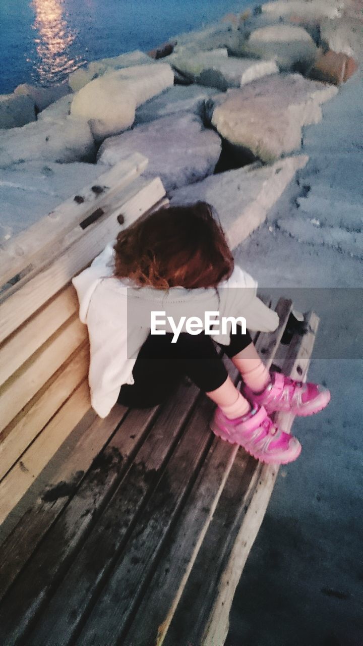 High angle view of sad girl sitting on bench at pier