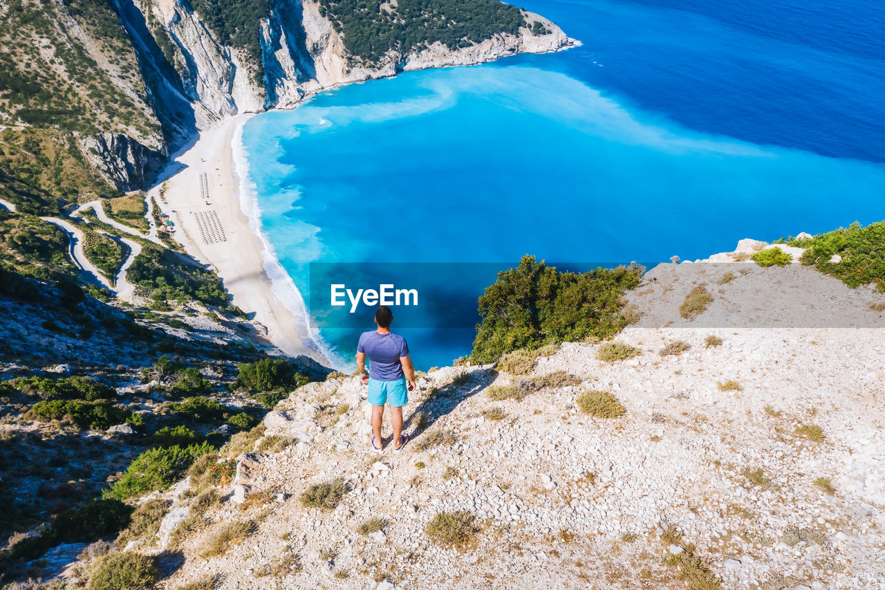 HIGH ANGLE VIEW OF MAN STANDING ON ROCKS AGAINST MOUNTAINS