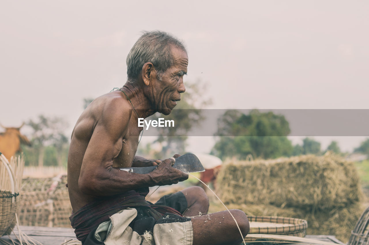 Side view of shirtless man sitting against clear sky