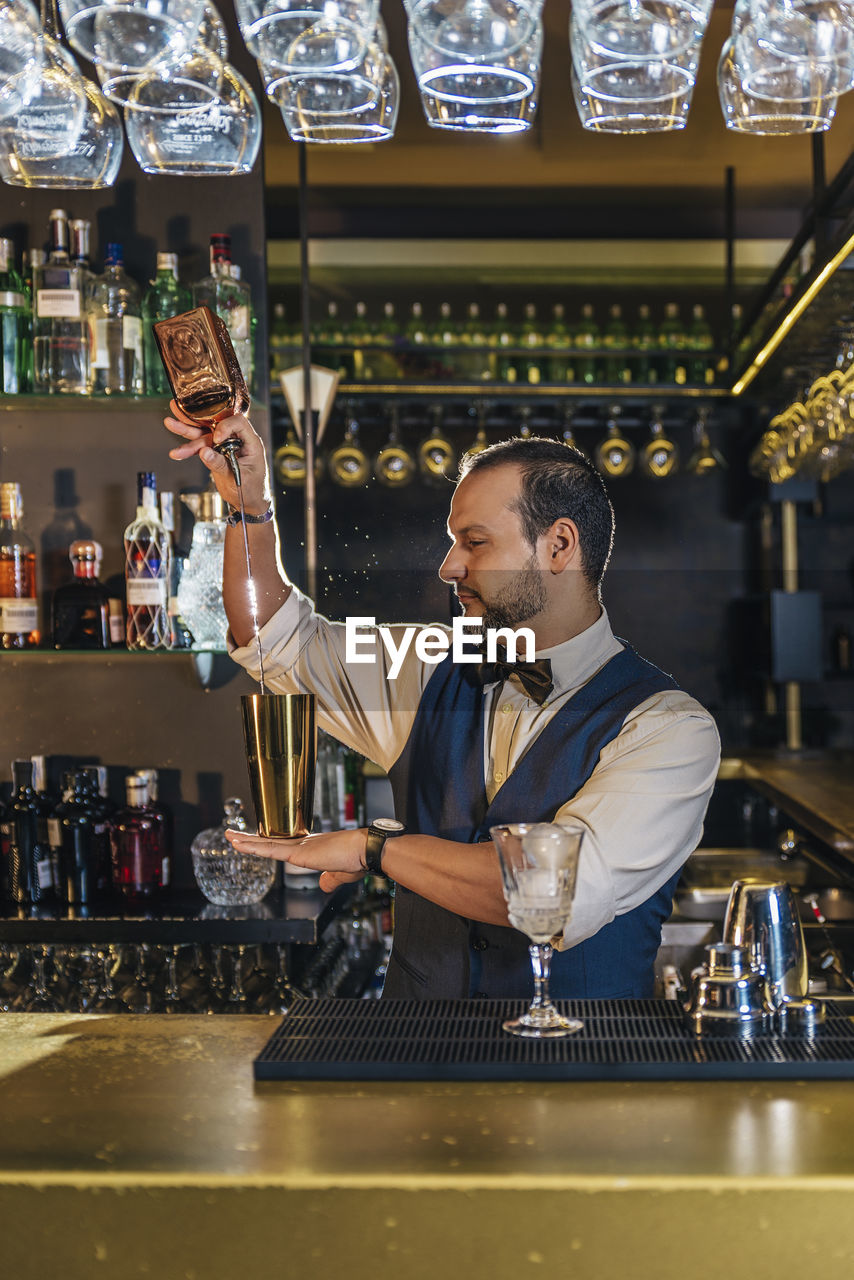 Bartender pouring drink in glass on counter at bar