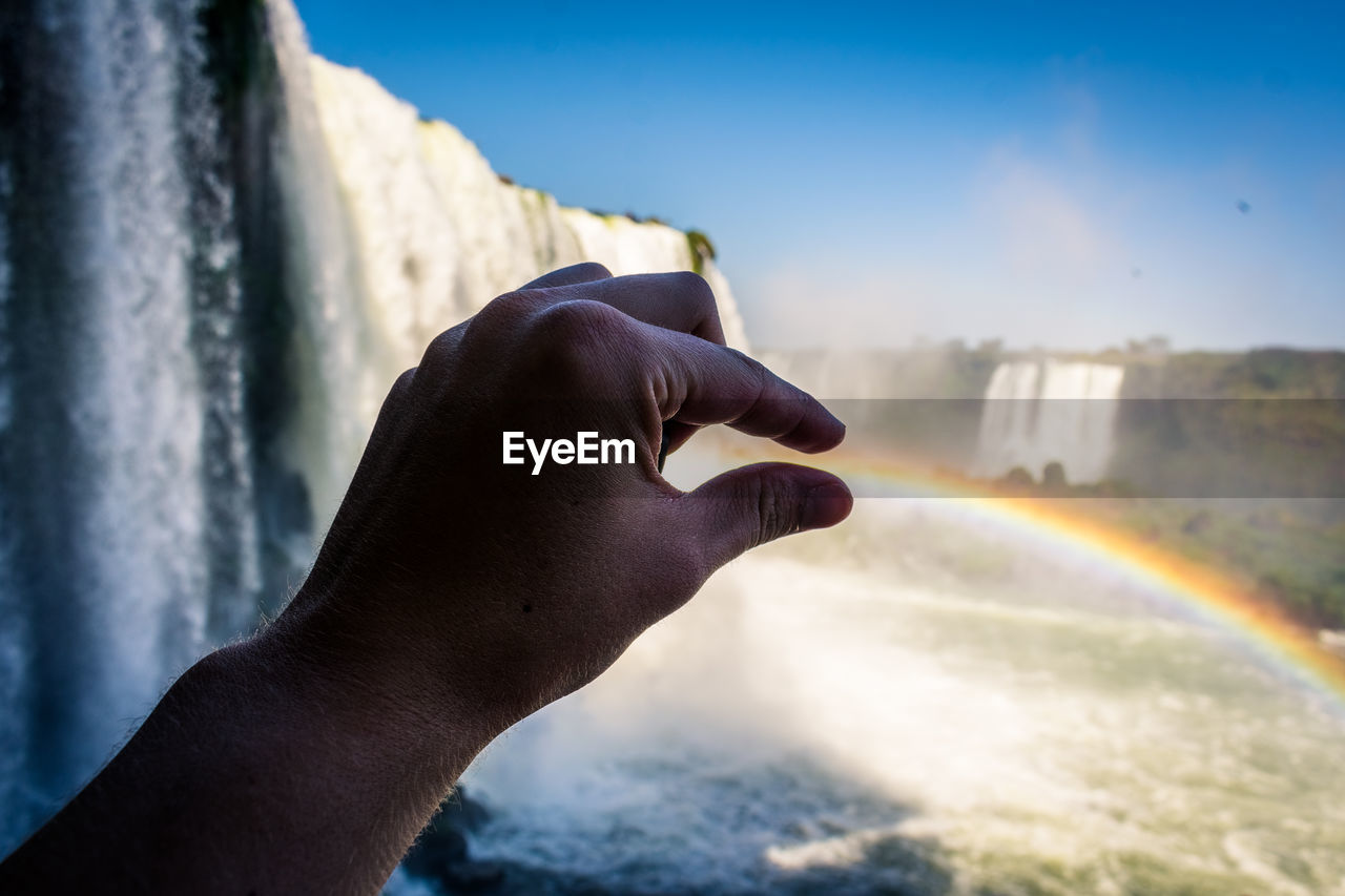 Close-up of hand rainbow by waterfall