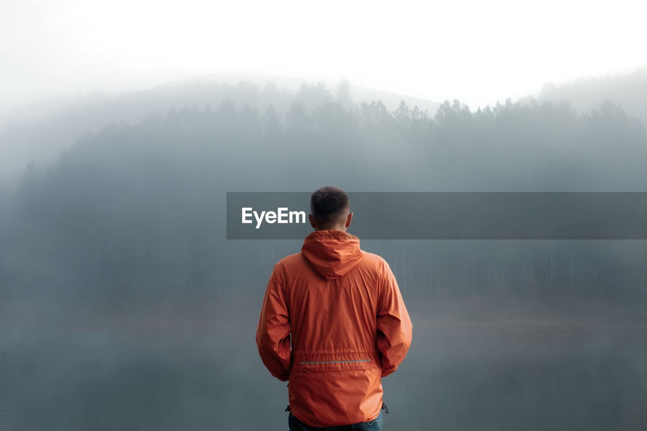 Man standing at lake during foggy weather 