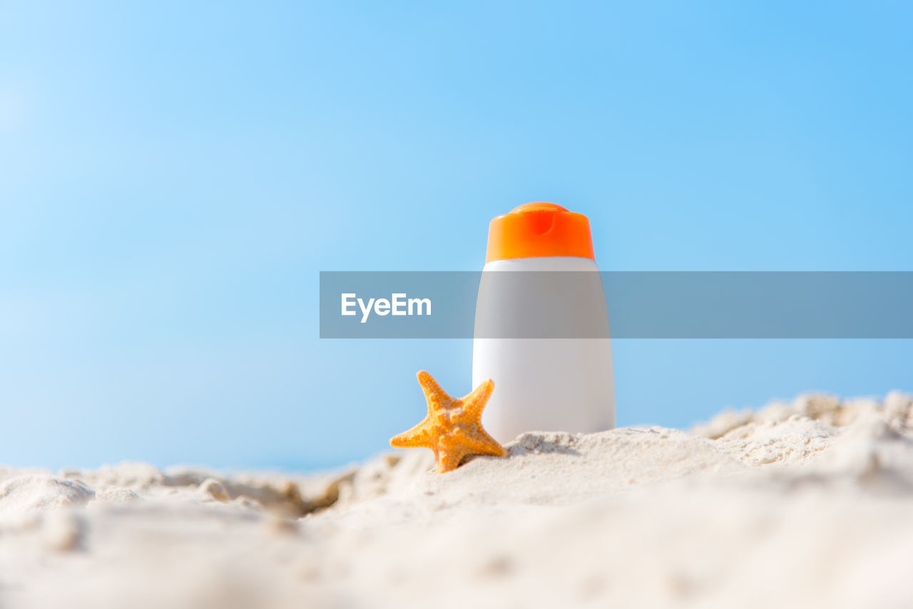 CLOSE-UP OF ORANGE LEAF ON SAND AGAINST SKY