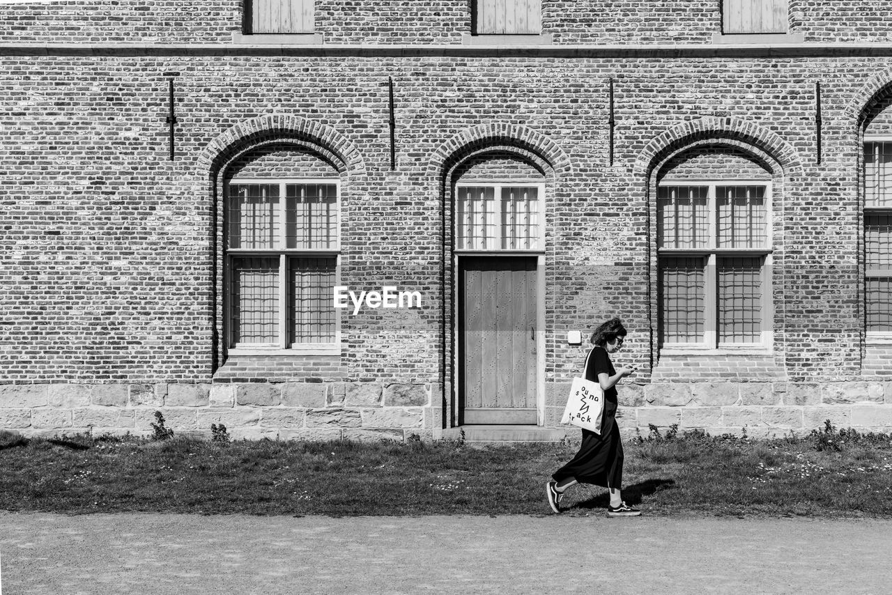 FULL LENGTH OF WOMAN STANDING BY BUILDING