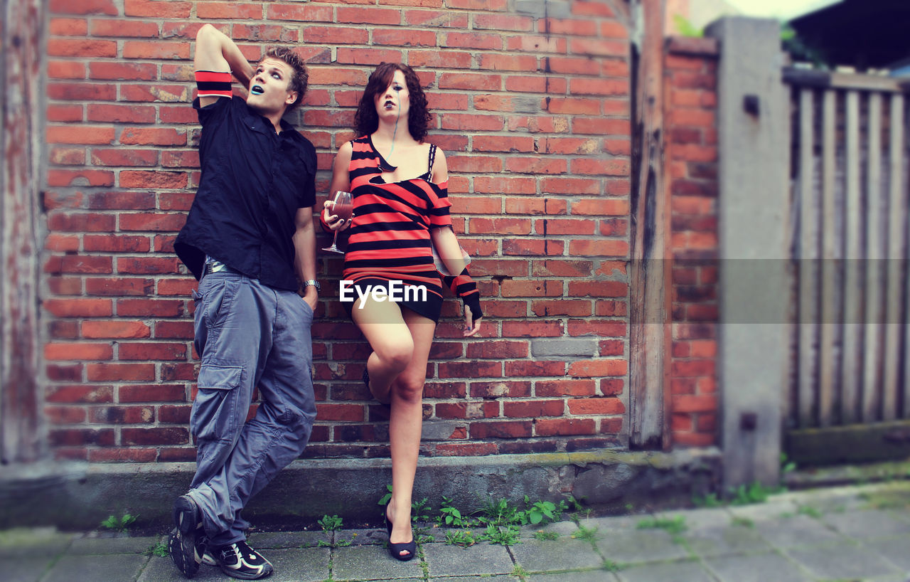 Full length of man and woman with halloween make-up standing against brick wall