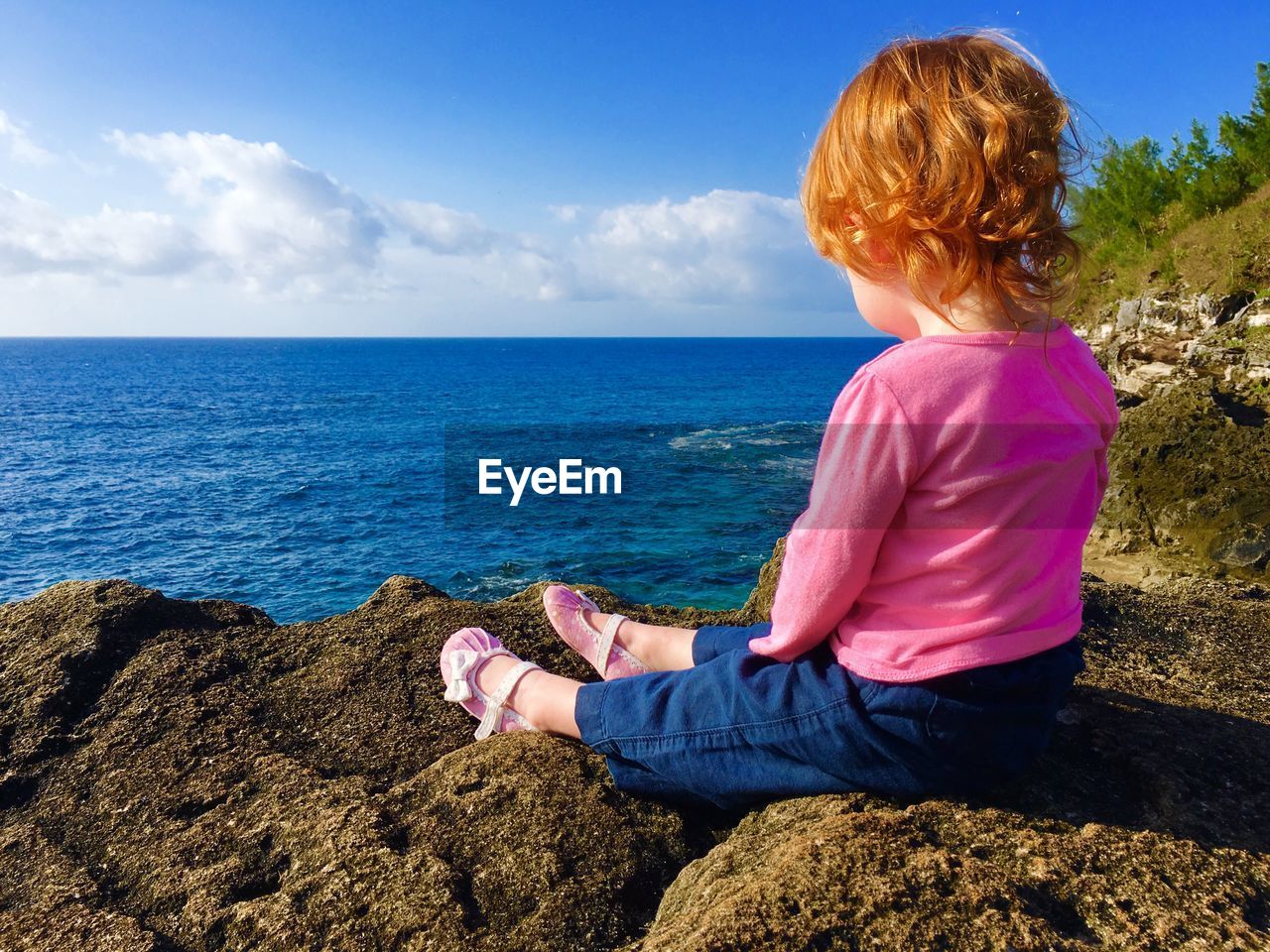 Full length of girl sitting on rock by sea against sky