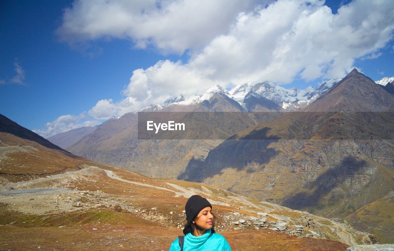 Mid adult woman sitting on mountain against cloudy sky during sunny day