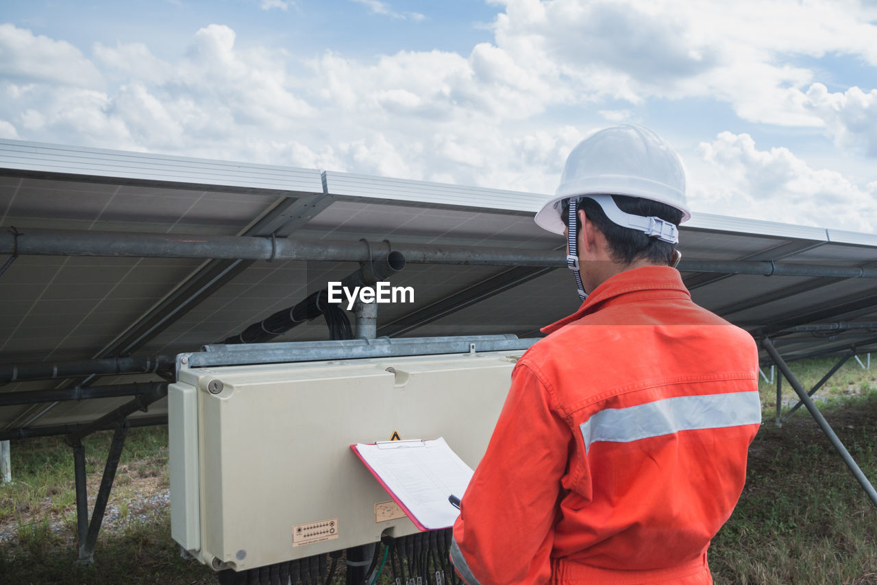 Side view of worker talking on phone while standing by solar panel