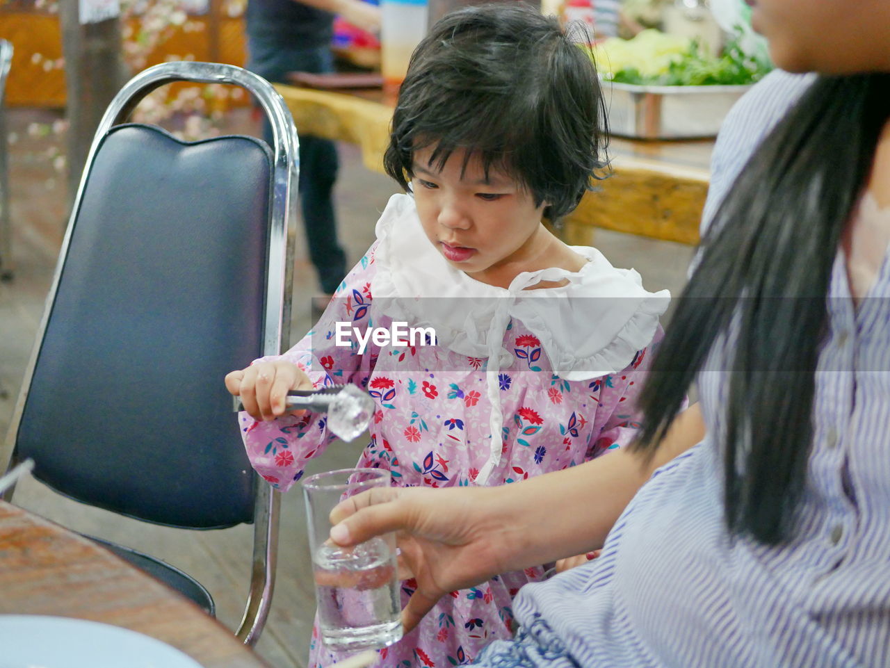 Cute girl putting ice cube in glass of water