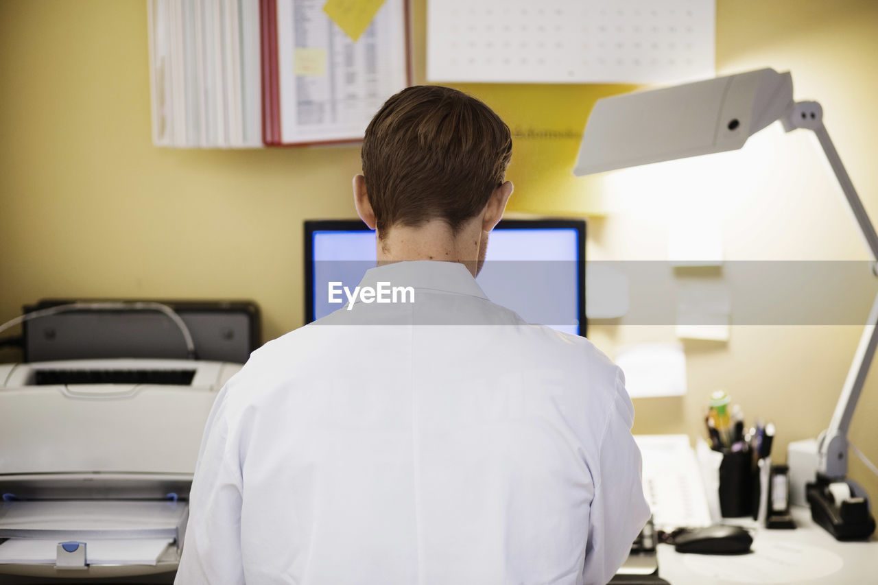 Rear view of mid adult male doctor using computer in clinic