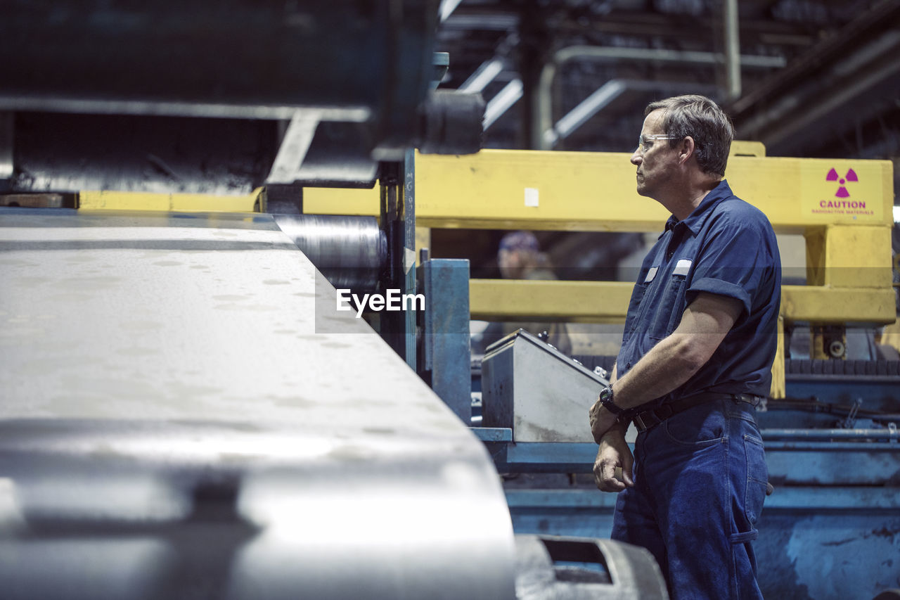 Manual worker looking at machine manufacturing sheet steel in factory