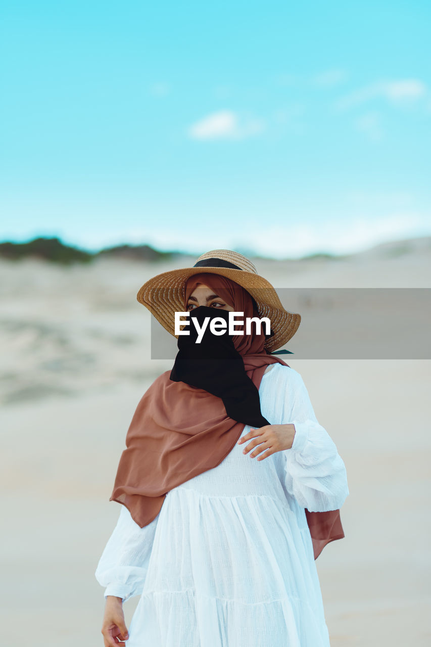 Muslim girl wearing hat, hijab and niqab walking in the desert against clear sky