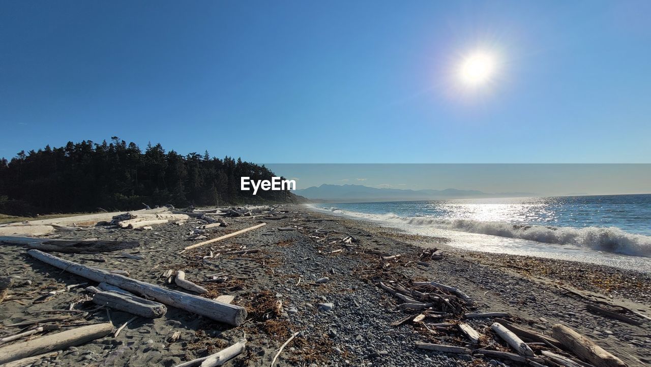 sky, sea, land, shore, coast, nature, water, beach, horizon, ocean, wave, scenics - nature, sunlight, beauty in nature, sun, tranquility, no people, tranquil scene, mountain, environment, blue, clear sky, body of water, outdoors, landscape, sunny, day, tree, non-urban scene, sand, travel, cloud, horizon over water, travel destinations, lens flare