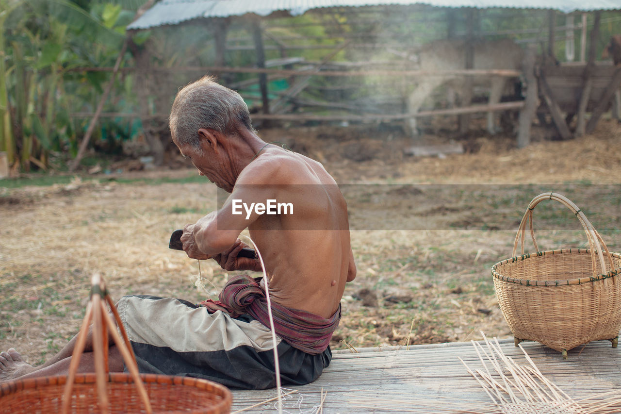 Shirtless senior man making straw basket