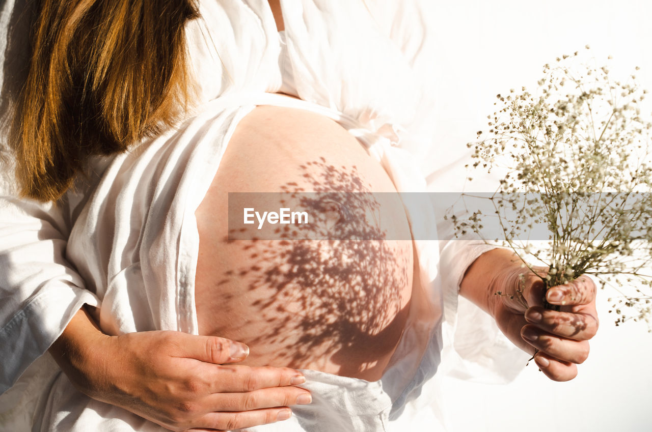  pregnant woman holding beautiful flowers having shadows on belly.pregnancy in spring,summer