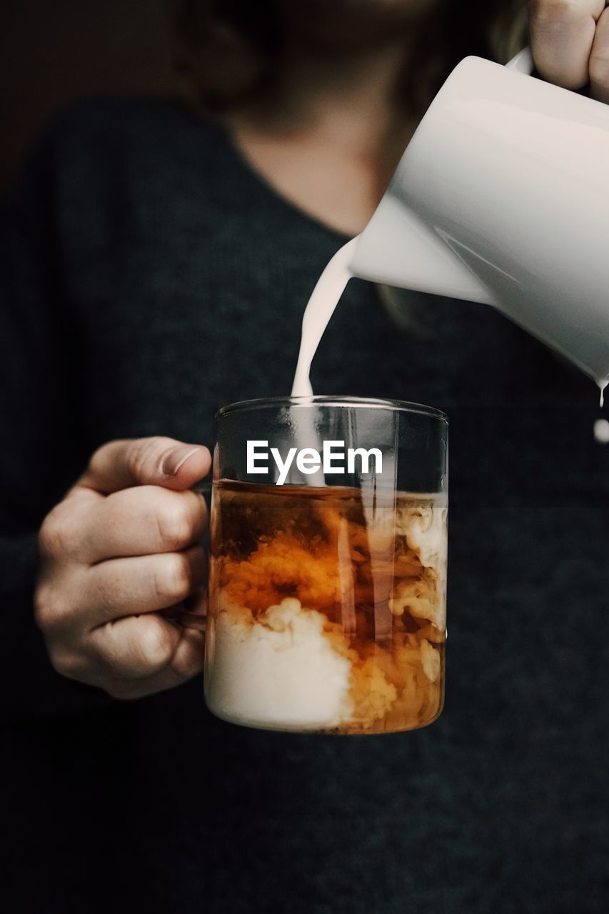 Midsection of woman pouring milk in coffee