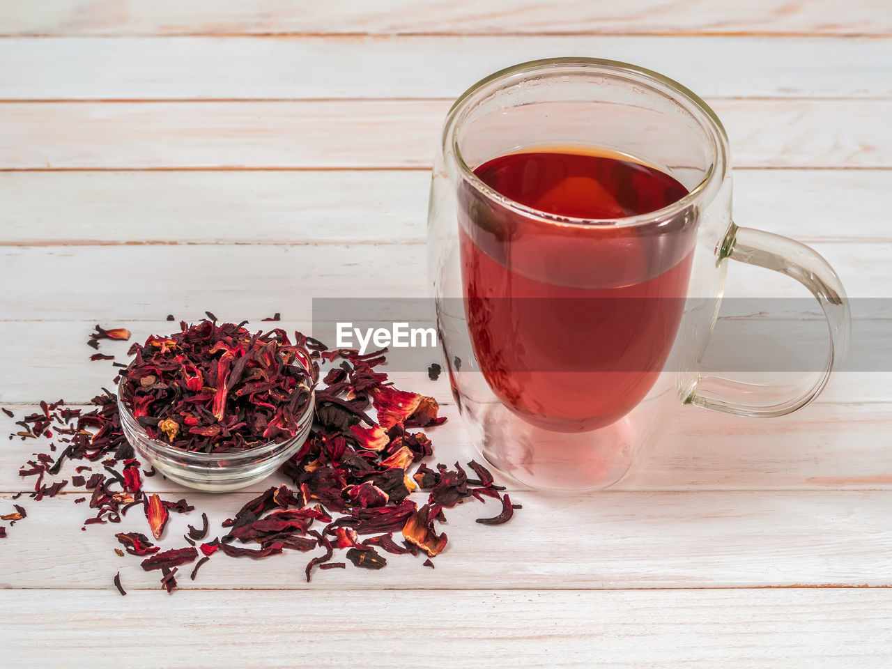 Clear double wall layer cup full of hot hibiscus tea with dry hibiscus leaves.