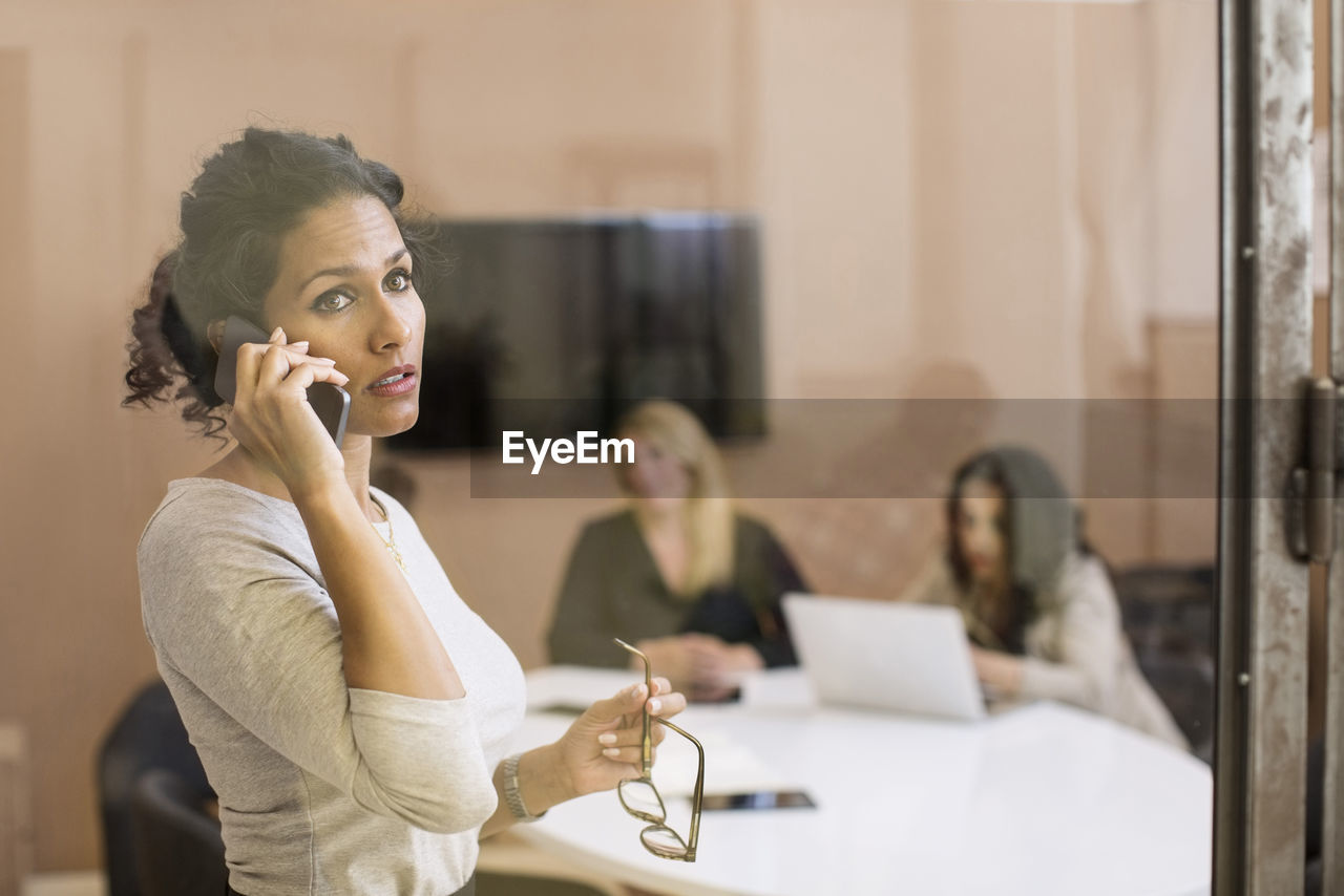 Businesswoman using mobile phone while looking away in creative office