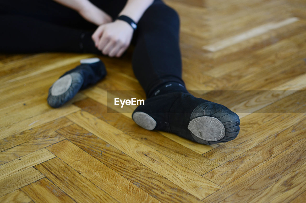 Low section of dancer sitting on hardwood floor