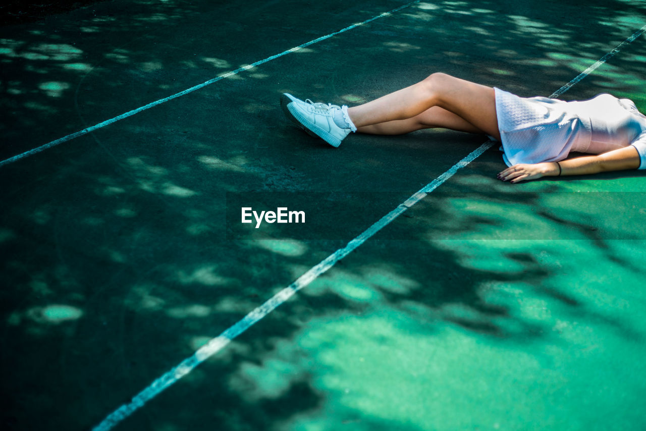 Low section of young woman lying on tennis court