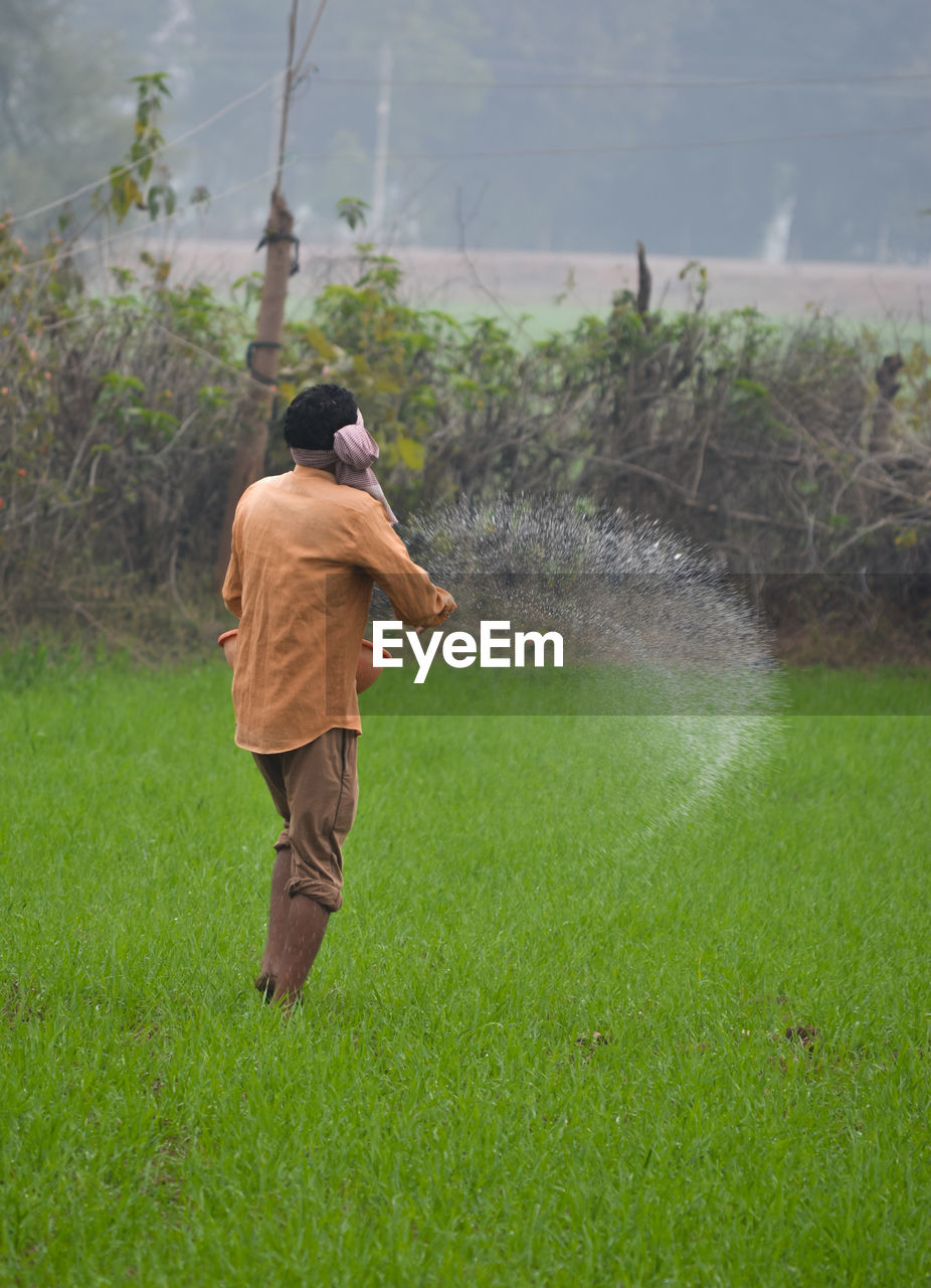 REAR VIEW OF MAN ON FIELD DURING RAINY DAY