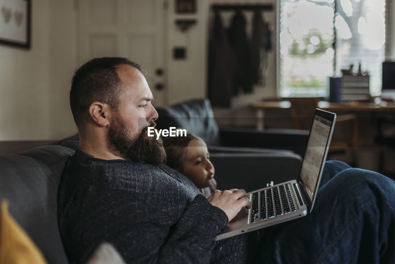 Close up of dad working from home with young daughter