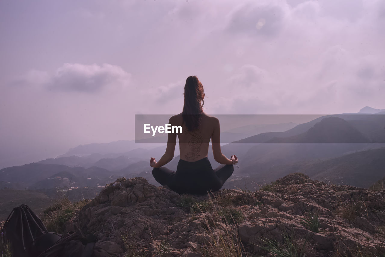 Woman meditating on mountain against sky