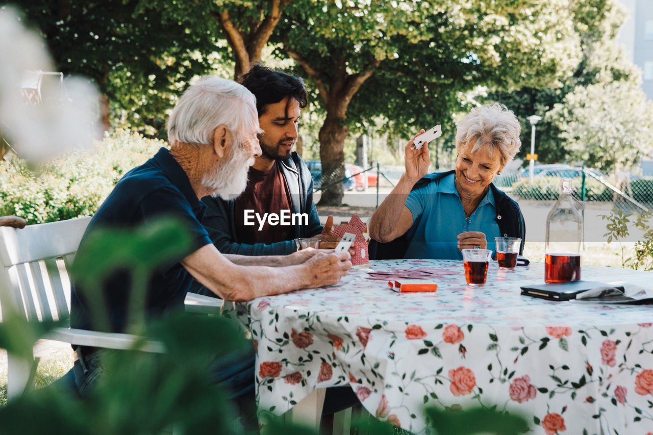 Cheerful senior woman playing cards with males at table in back yard