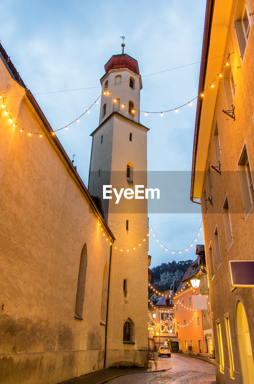 LOW ANGLE VIEW OF ILLUMINATED CLOCK TOWER AMIDST BUILDINGS IN CITY