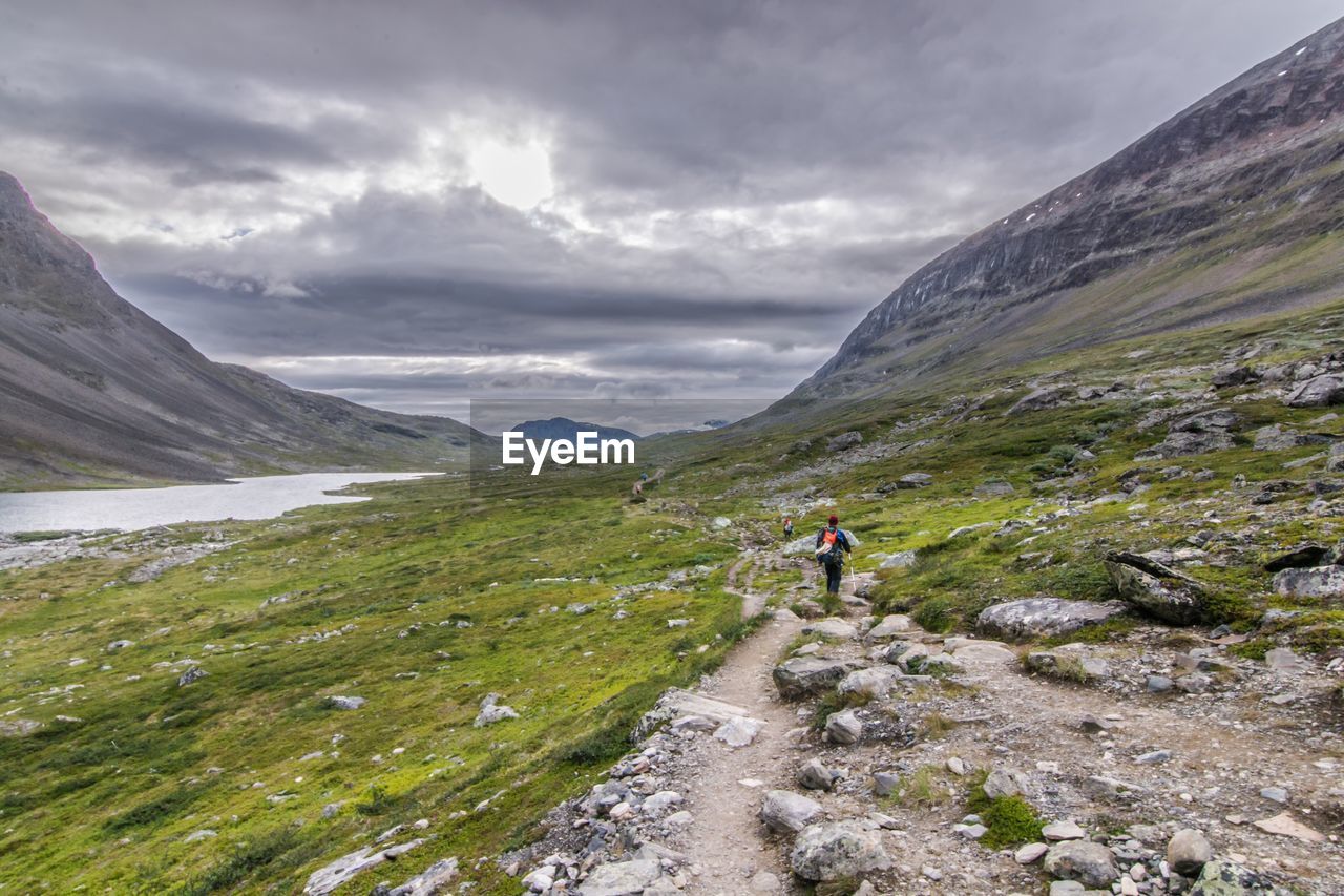 Rear view of person hiking on mountains against cloudy sky