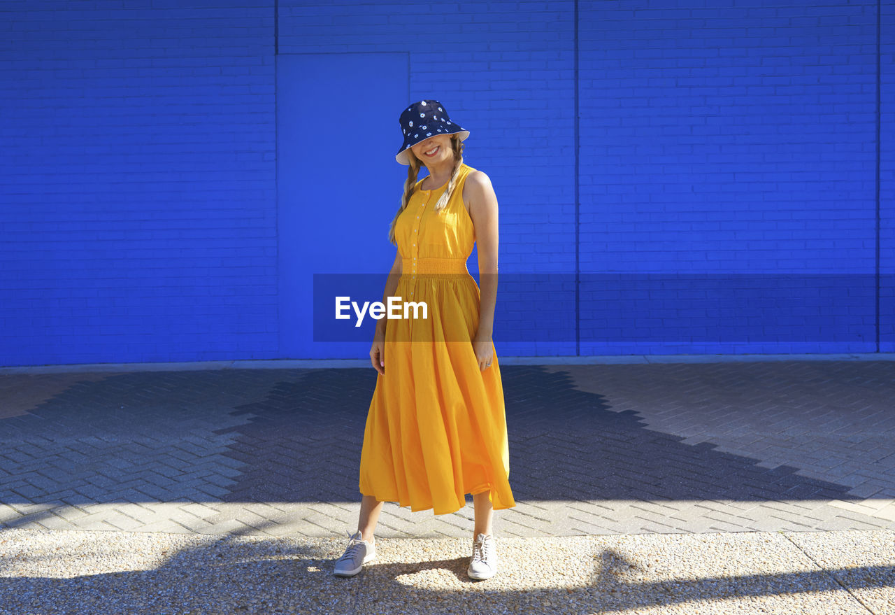 Mature woman wearing bucket hat standing in front of wall on sunny day