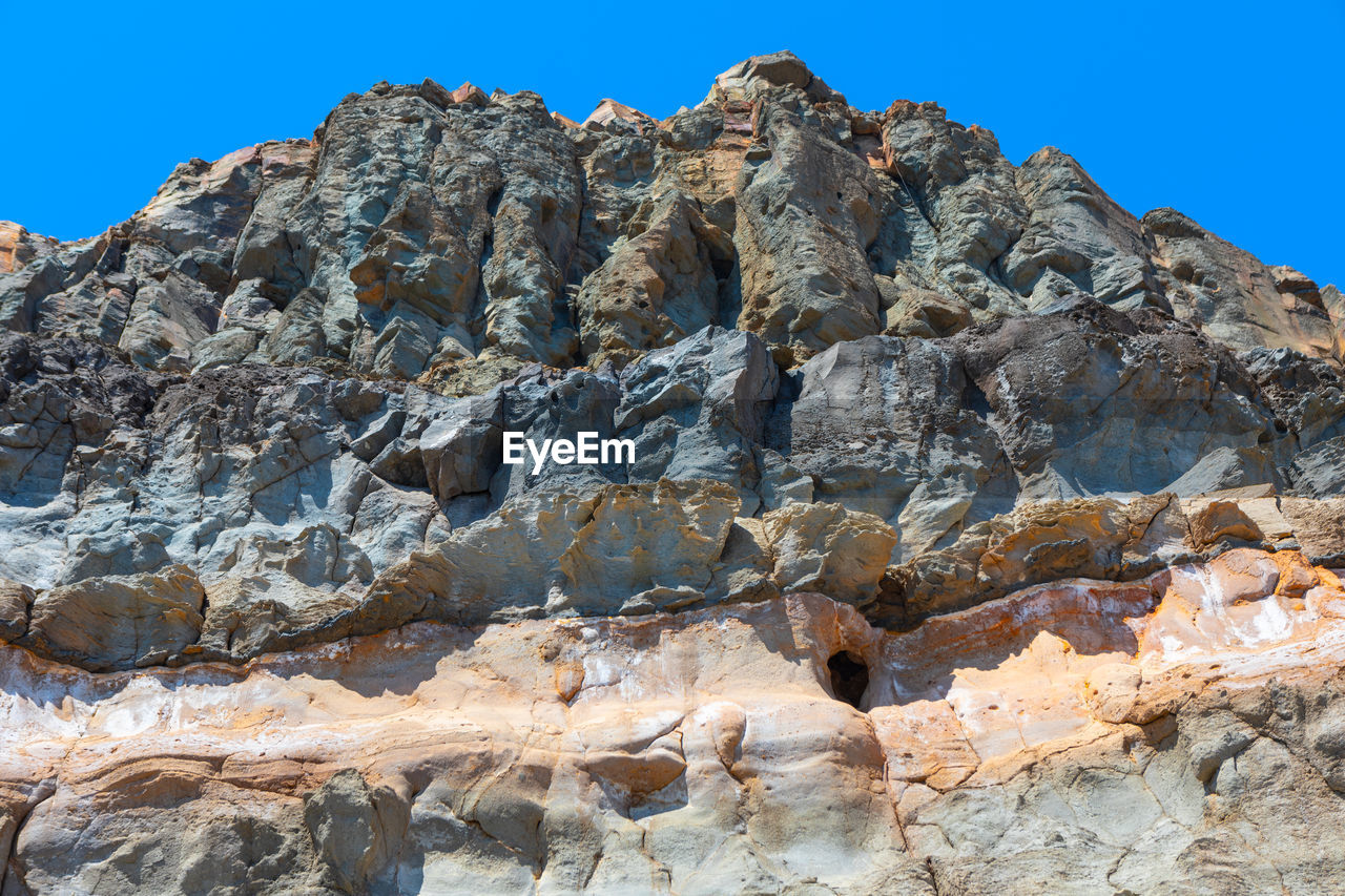 rock, nature, sky, mountain, rock formation, geology, scenics - nature, blue, environment, beauty in nature, formation, clear sky, landscape, land, no people, travel destinations, terrain, travel, outdoors, cliff, day, non-urban scene, mountain range, sunny, extreme terrain, ridge, physical geography, wadi, low angle view, wilderness, sunlight, tranquility, eroded