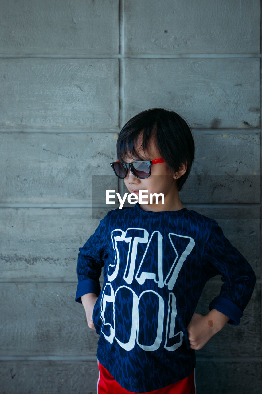 Boy with hands on hip standing against wall