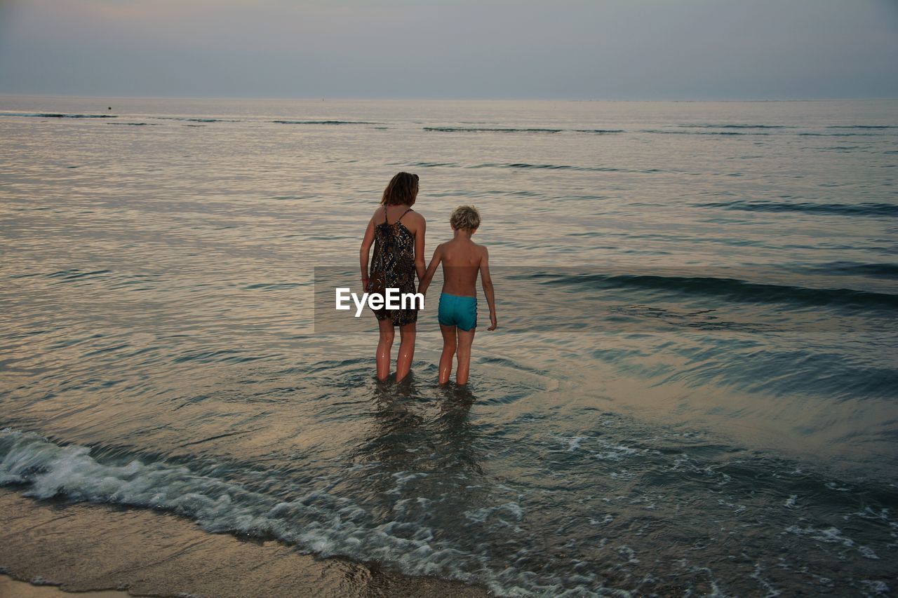 Mother and son wading in sea during sunset