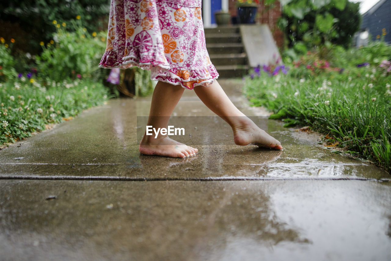 Close-up of a small barefoot child dancing on front stoop in the rain