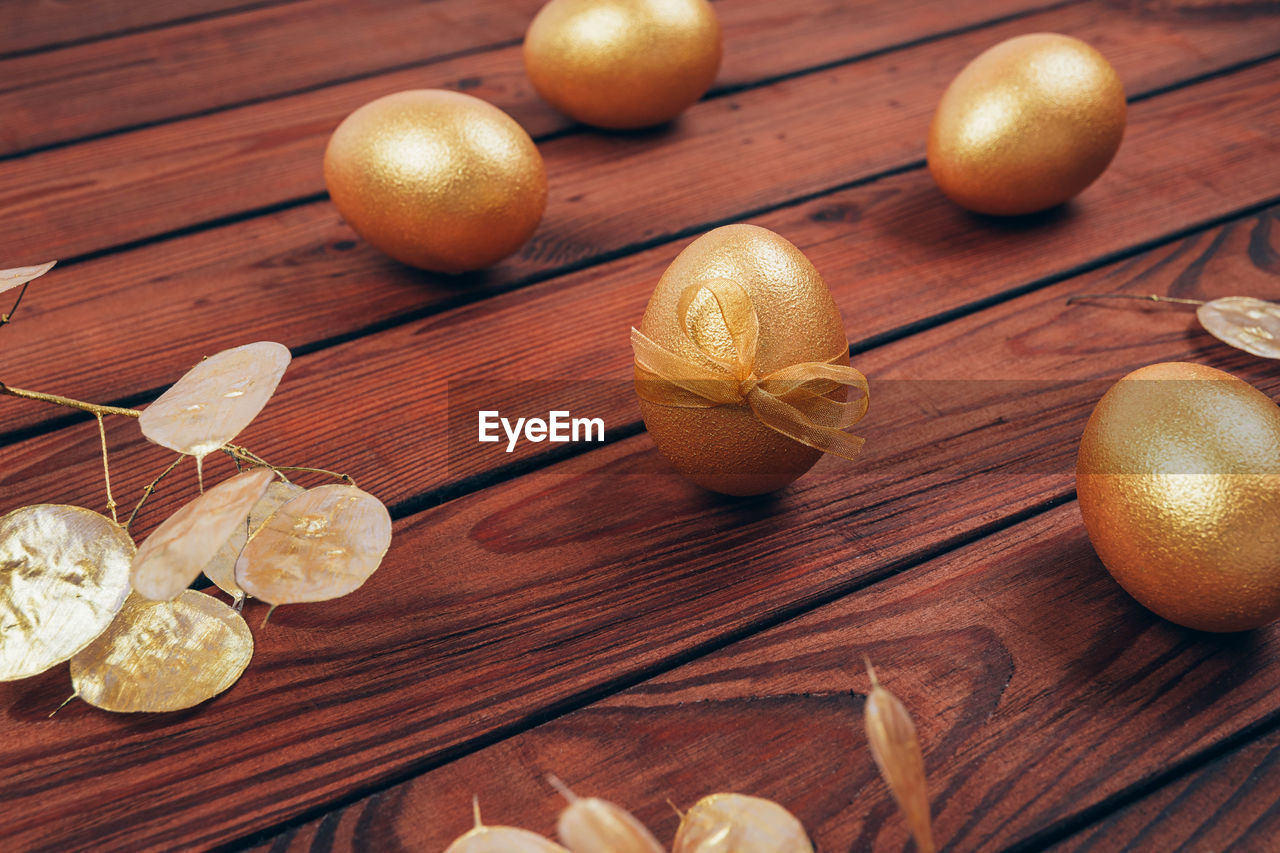 Golden colored easter eggs with dry flowers over dark wooden planked background 