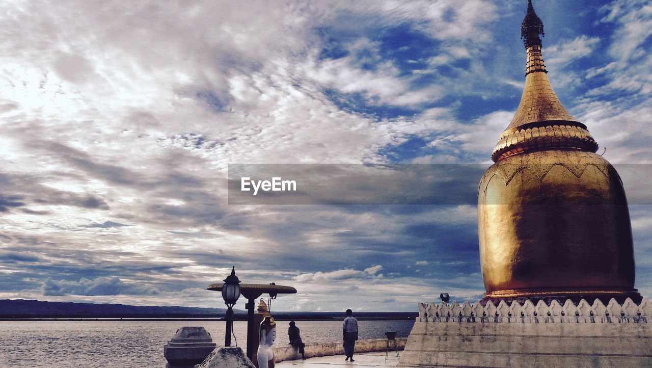 Golden stupa by river against cloudy sky