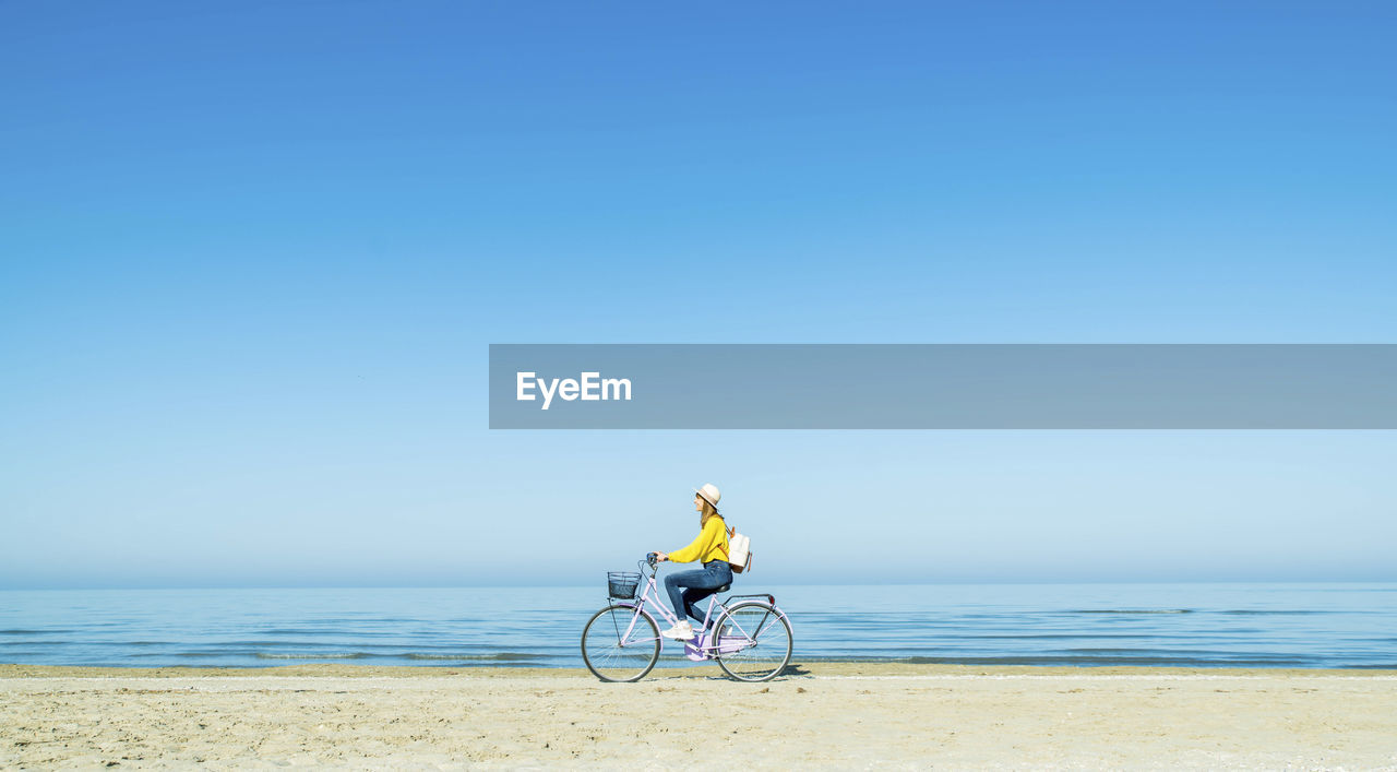 Young woman riding bicycle at beach on sunny day
