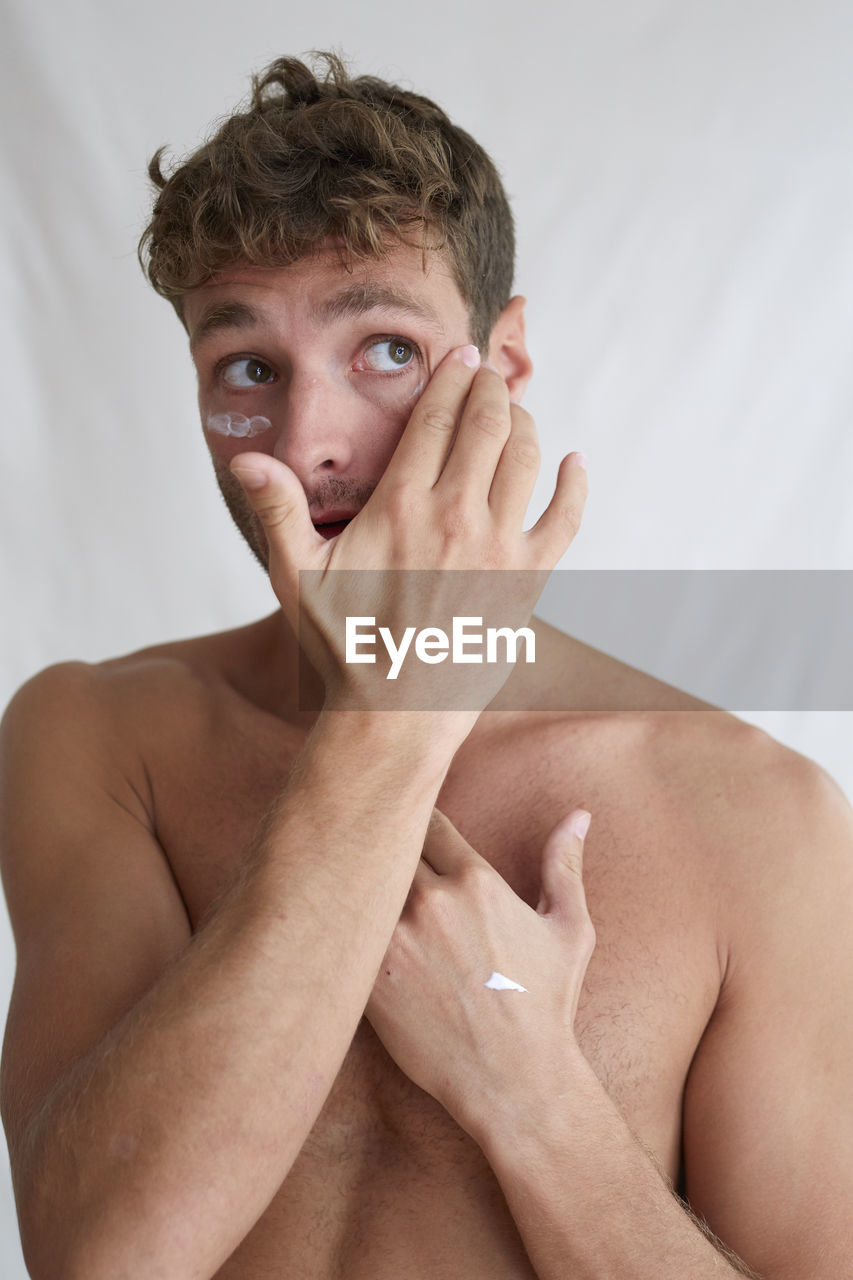 PORTRAIT OF SHIRTLESS YOUNG MAN OVER WHITE BACKGROUND