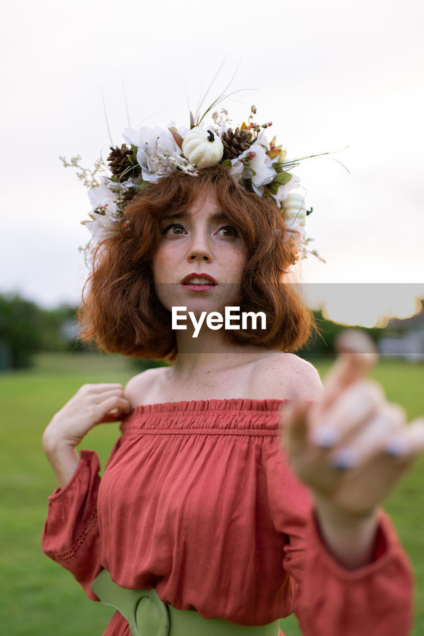 Woman wearing flowers while standing on land against sky during sunset