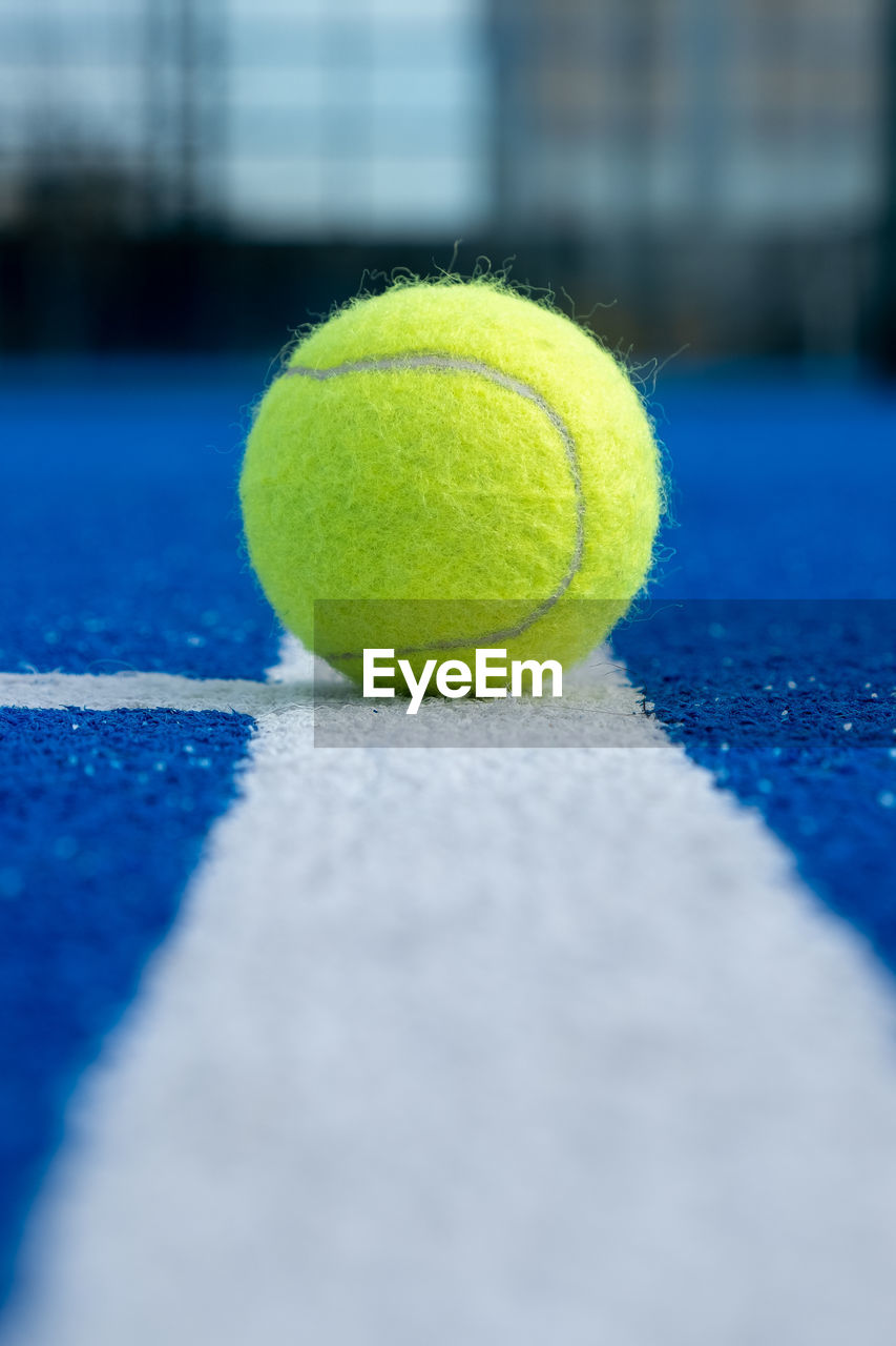 Selective focus of a ball on the white line of a blue paddle tennis court
