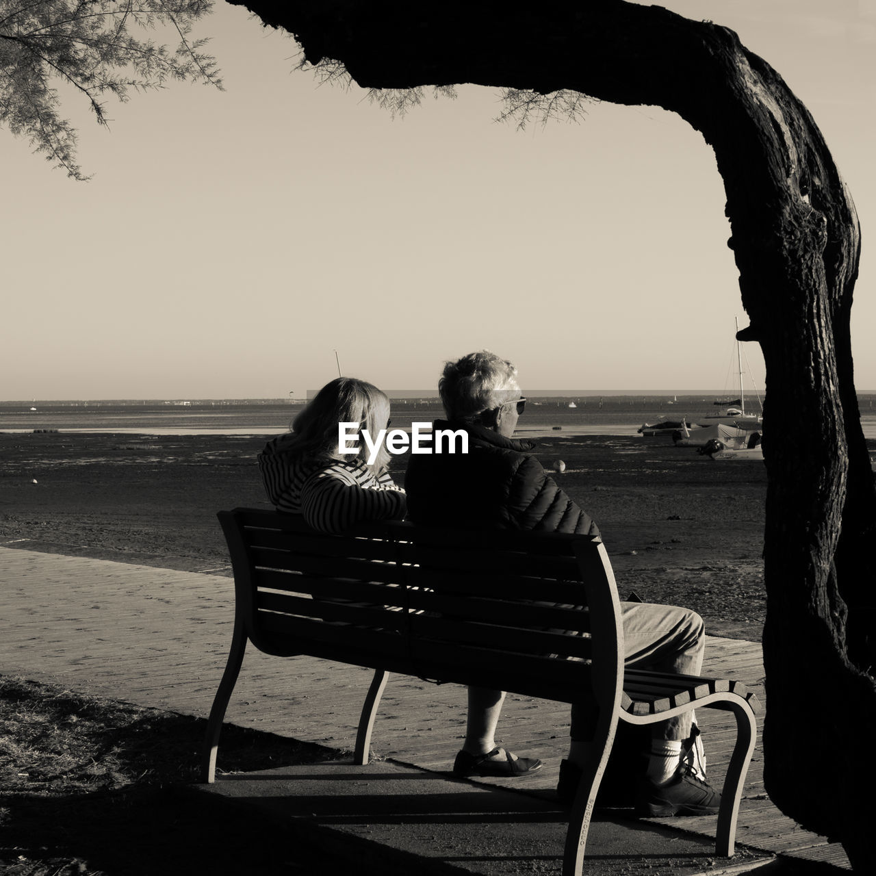 REAR VIEW OF WOMAN SITTING ON BEACH LOOKING AT SEA