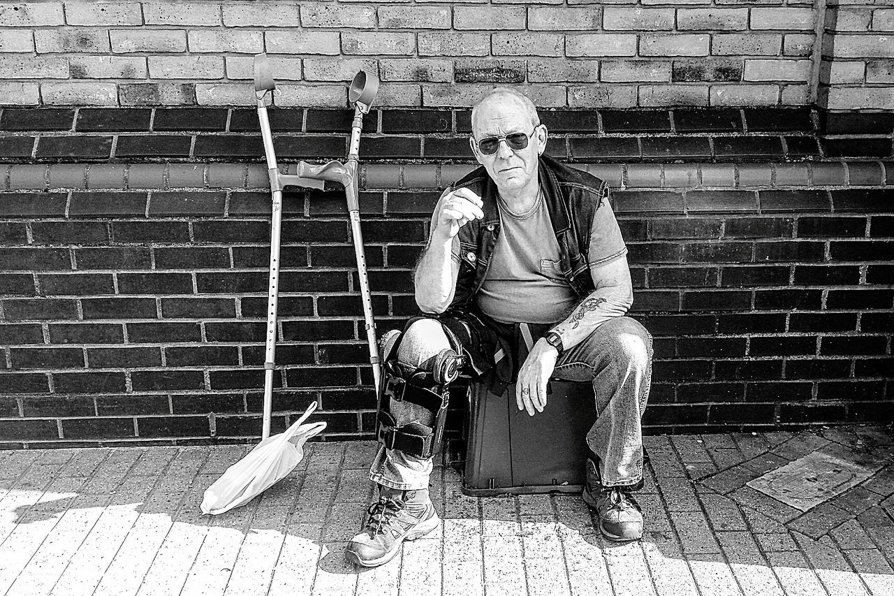 Portrait of man sitting on box against brick wall