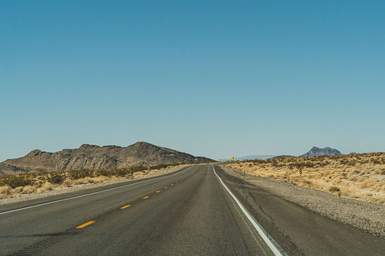 Two lane desert highway in nevada road leading to the horizon against clear blue sky and mountains