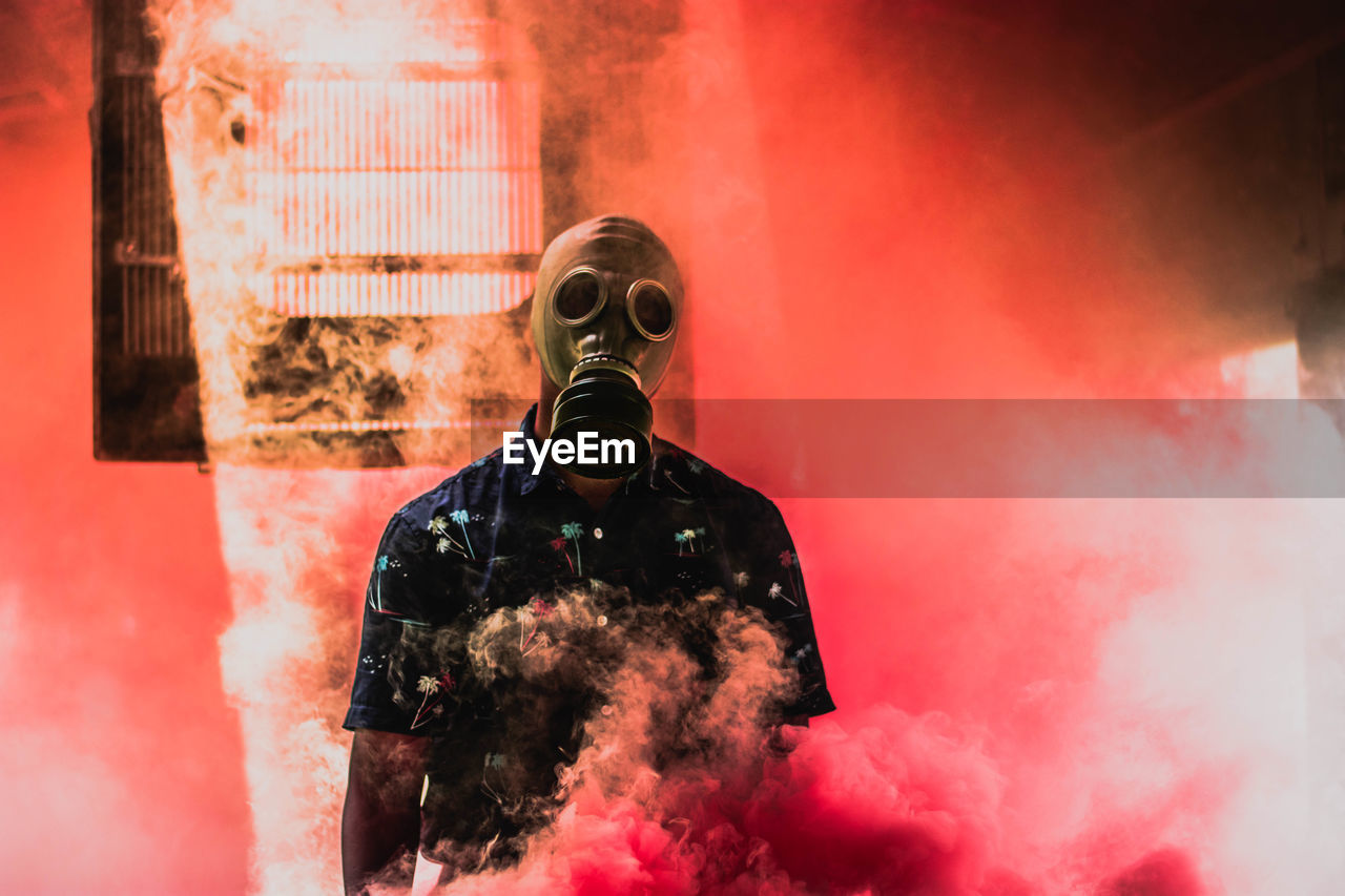 Teenage boy wearing gas mask while standing amidst smoke