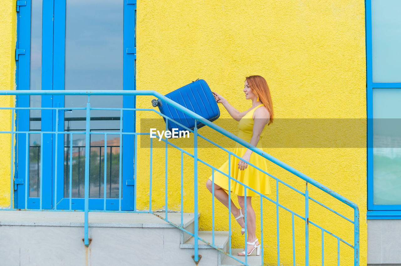 SIDE VIEW OF WOMAN WITH UMBRELLA AGAINST YELLOW METAL RAILING