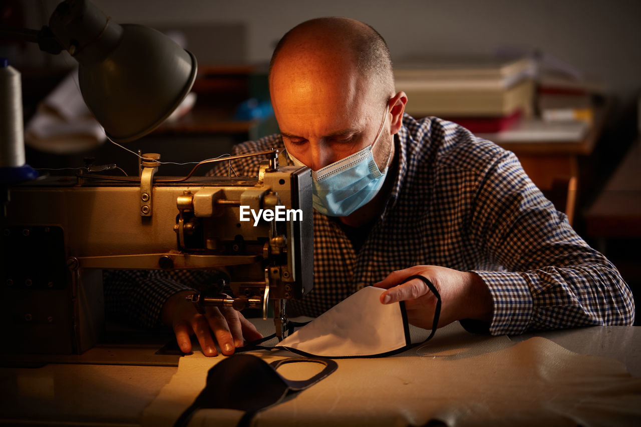 Man sewing mask with machine on table